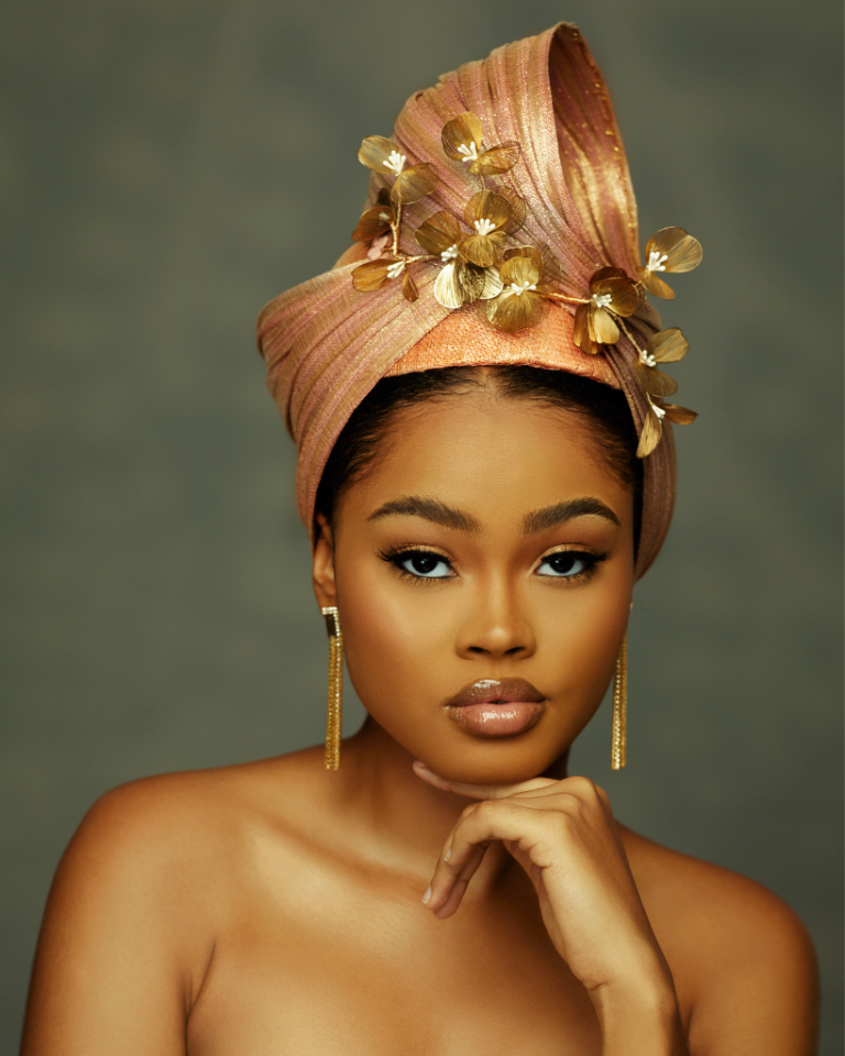 Ashanti: A detailed handcrafted turban made with sinamay, buntal and metallic flowers. Color: peach and gold