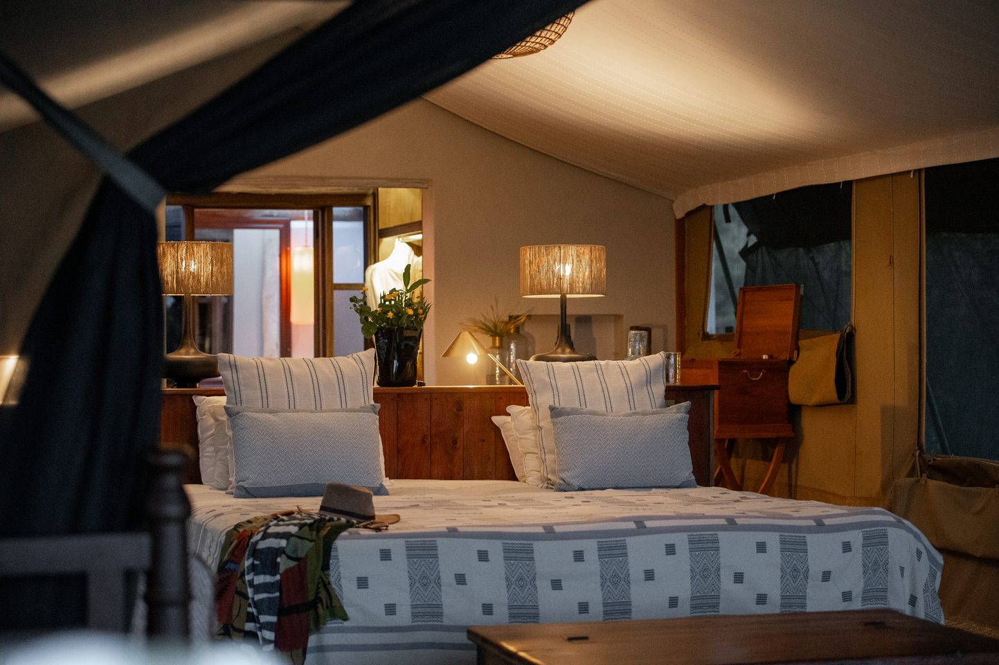 Tented Suite Interior Bedroom: A detailed look inside one of the eight refreshed tented suites at River Camp Mara. The design overhaul has upgraded guest comfort while preserving the camp's historic safari soul, utilizing artisanal fabrics and traditional patterns. Photo Credit: Hemingways Collection